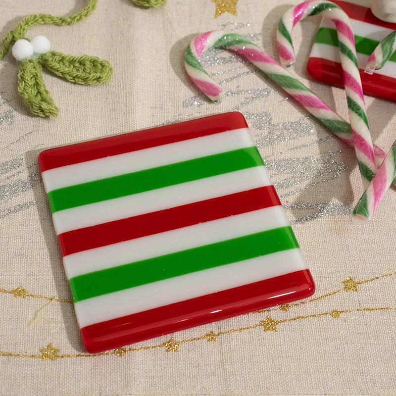 Festive red, green, and white striped glass coaster with candy canes on holiday tablecloth