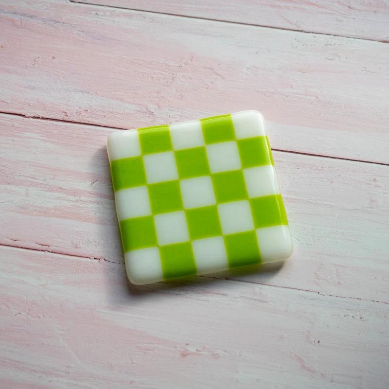 Green and white checkered glass coaster on pink wood, handmade British craft